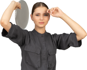 Front view of a young woman in a jumpsuit holding glass plate