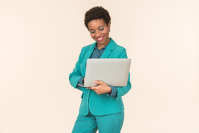 Jeune femme noire avec une coupe de cheveux courte, posant dans un costume bleu avec un ordinateur portable dans ses mains