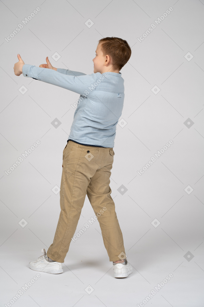 Вид сзади на мальчика, показывающего большие пальцы вверх