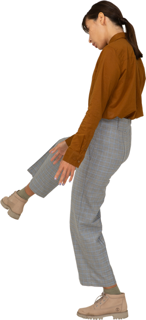 Vista traseira a três quartos de uma jovem mulher asiática de calça e blusa levantando a perna