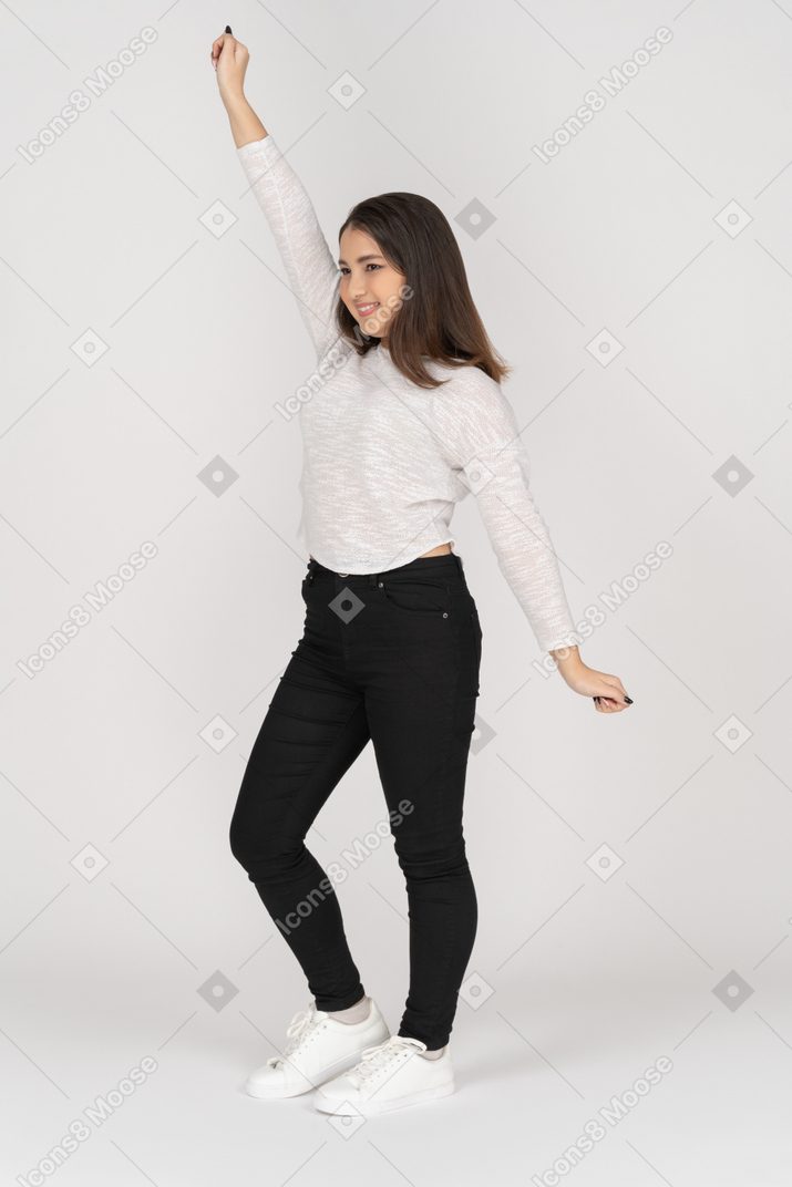 Three-quarter view of a smiling young dancing indian female in casual clothes raising hand