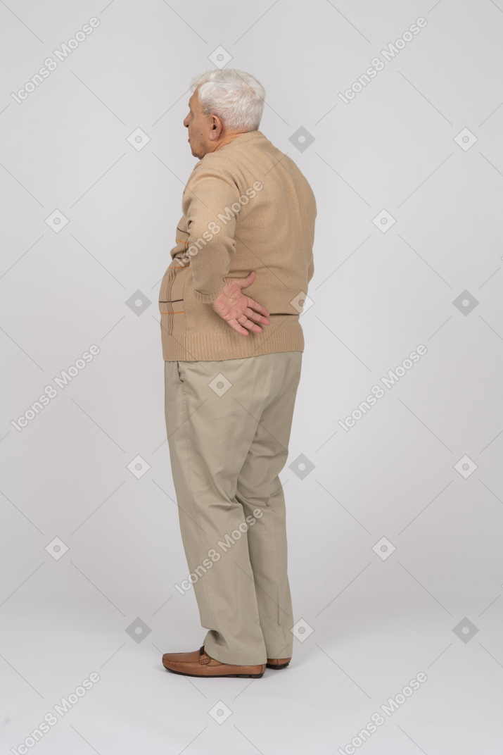 Vista lateral de um velho em roupas casuais, sofrendo de dor nas costas