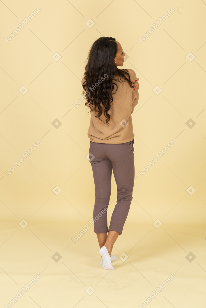 Back view of a dark-skinned pleased young female embracing herself
