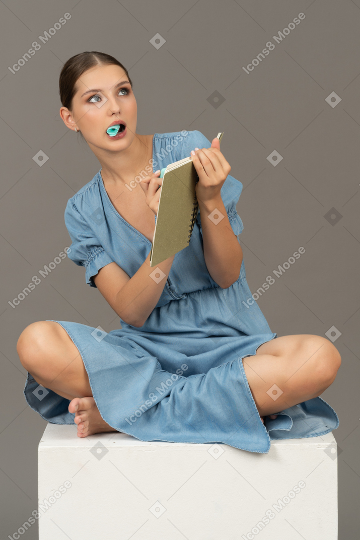 Vista frontale della giovane donna seduta su un cubo con pennarello e taccuino