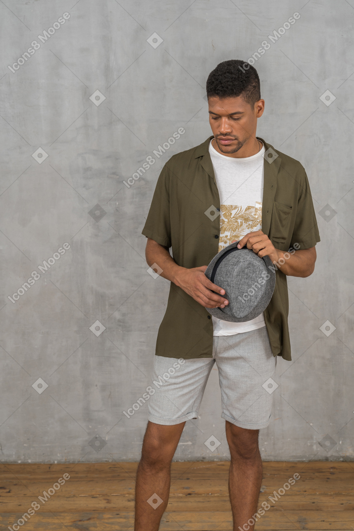 Hombre con ropa informal mirando hacia abajo mientras sostiene el sombrero