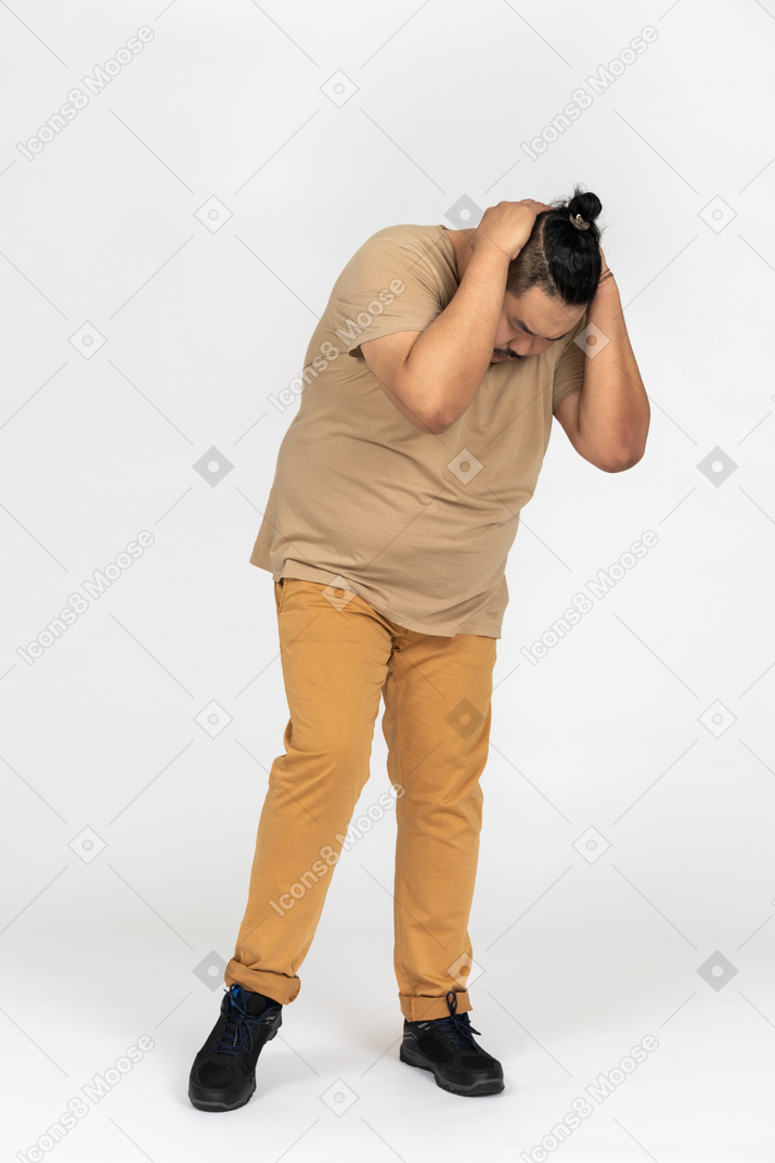 Hombre asiático de talla grande inclinándose y sosteniendo su cabeza mientras sufre de dolor de cabeza intenso