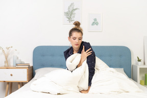 Front view of a tired young woman in pajamas touching her arm while staying in bed