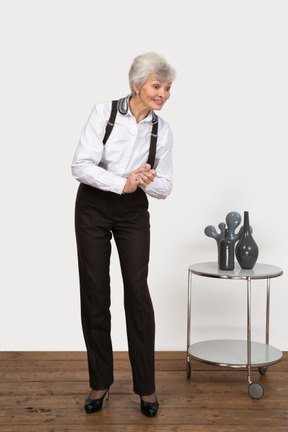 Vorderansicht einer erfreuten alten dame in bürokleidung, die hände zusammenhält