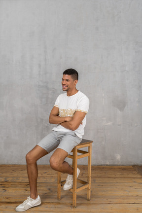 Lächelnder mann, der mit verschränkten armen auf einem stuhl sitzt