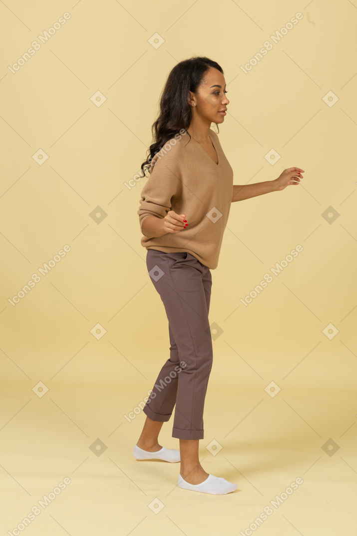 Three-quarter view of a dark-skinned walking young female outspreading her hands