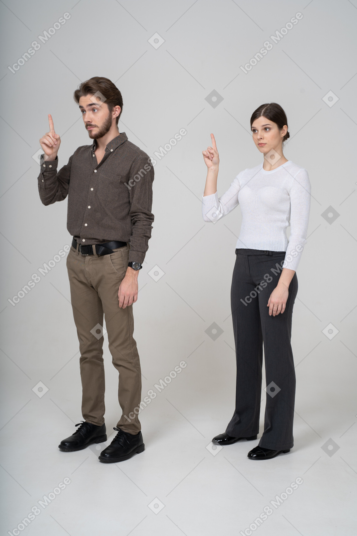 Vista de tres cuartos de una pareja joven en ropa de oficina levantando el dedo