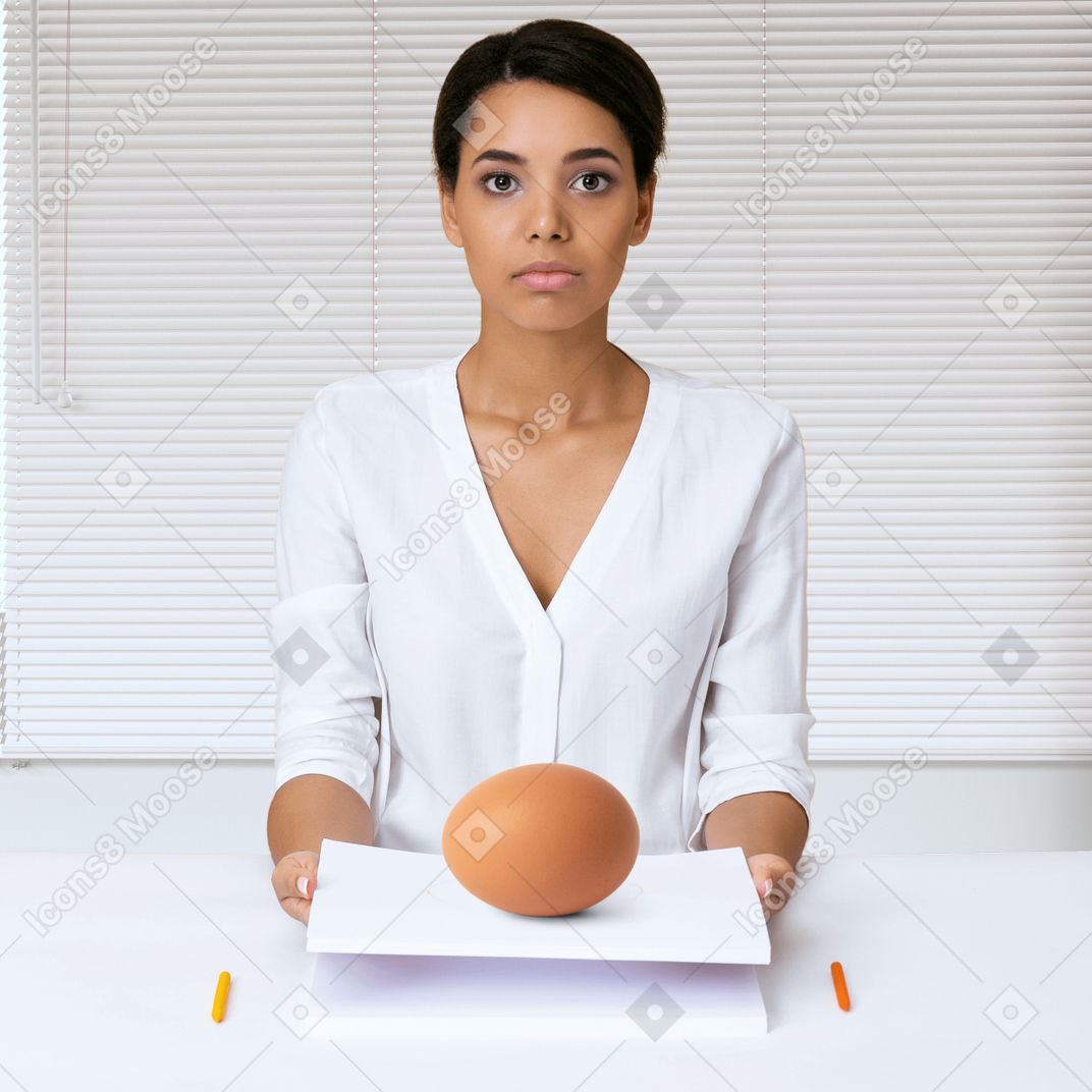 A woman sitting at a desk with an egg in front of her