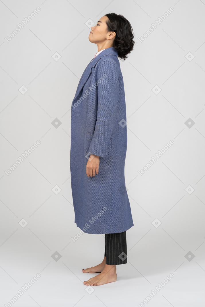 Angry looking young woman in long blue coat standing in profile