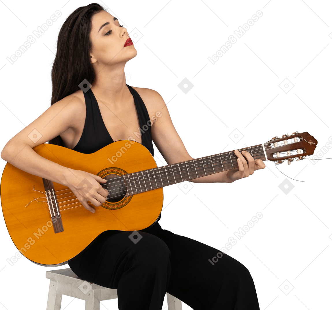 Vista de três quartos de uma jovem sentada de terno preto segurando o violão e erguendo a cabeça