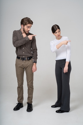 Vista frontal de um jovem casal com roupas de escritório apontando para a direita