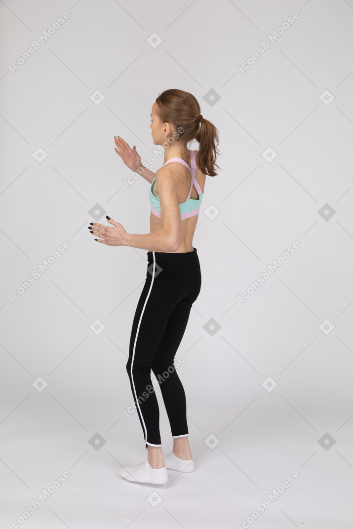Three-quarter back view of a teen girl in sportswear standing like a robot