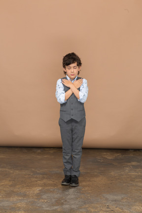 Вид спереди на симпатичного мальчика в сером костюме, стоящего с руками на плечах