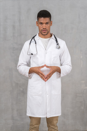 A man in a white lab coat standing with his hands touching