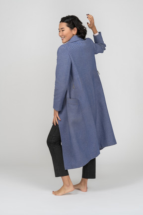 Vista posteriore di una donna allegra in cappotto con la mano in alto