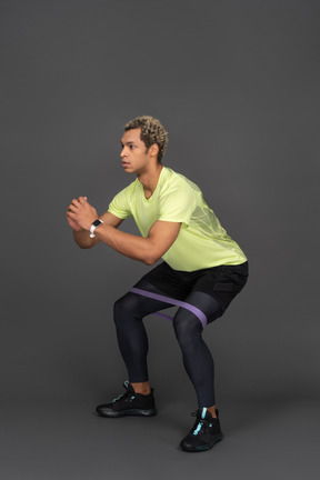 Three-quarter view of a dark-skinned young man squatting with an elastic rubber