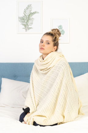 Three-quarter view of a young lady wrapped in white blanket sitting in bed