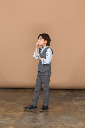 Vista lateral de un niño con traje gris pellizcando la nariz