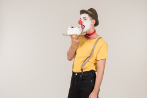 Male clown licking the cake he's holding