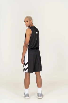 Vista posterior de un joven jugador de baloncesto masculino sospechoso girando la cabeza y mirando a la cámara