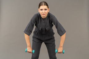 Вид спереди молодой женщины в комбинезоне, делающей упражнения с гантелями