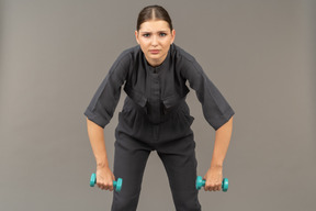 Front view of young woman in a jumpsuit doing exercises with dumbbells