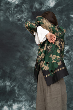Foto a três quartos de mulher jovem em jaqueta de seda escondendo o rosto