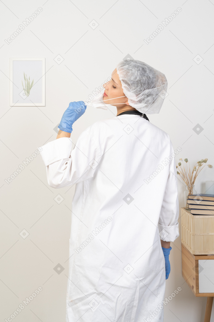 Back view of a young female doctor trying to take mask off