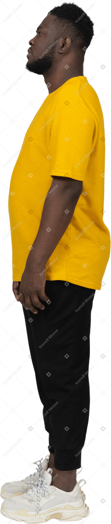 Vista lateral de un joven de piel oscura con camiseta amarilla parado
