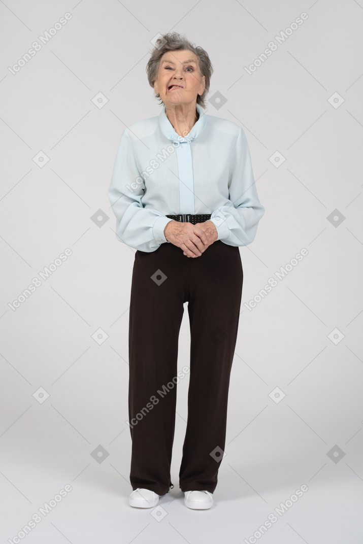 Front view of an old woman grimacing with hands clasped