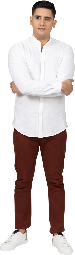 Front view of a young latino man holding his elbows and looking aside distractedly