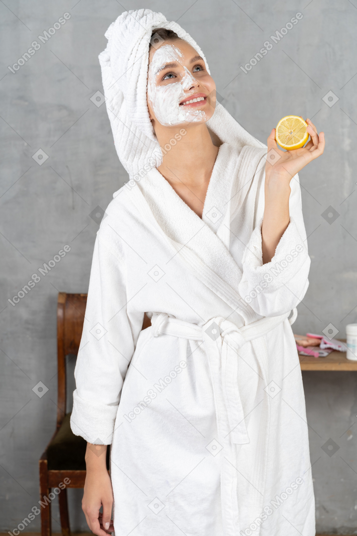Souriante jeune femme en peignoir tenant un citron