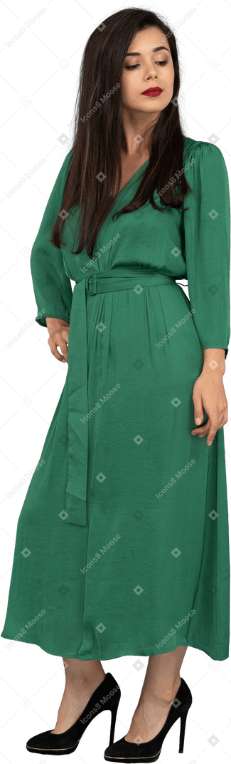 Vue de trois quarts d'une fière jeune femme en robe verte mettant la main sur la hanche