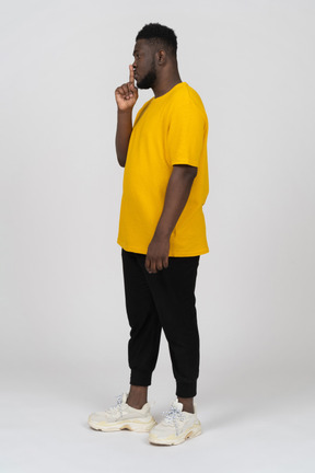 一个身穿黄色 t 恤的黑皮肤年轻男子表现出沉默手势的四分之三视图