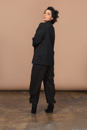 Vista traseira de uma empresária em um terno preto mostrando a língua e olhando para a câmera