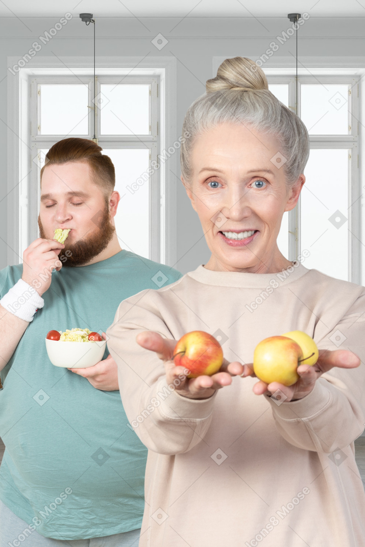 A woman holding apples and a man eating a salad
