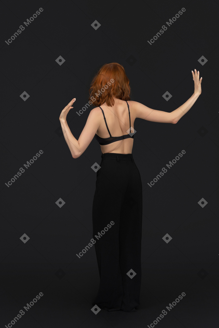 A backside view of the cute young woman dancing on the black background