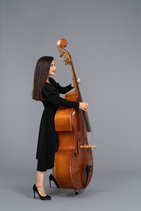 Vista laterale di una giovane musicista di sesso femminile in abito nero che tiene il suo contrabbasso