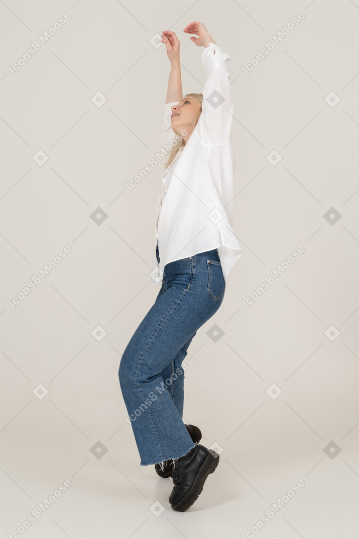 Vista lateral de una mujer bailando en ropa casual levantando las manos y doblando la rodilla