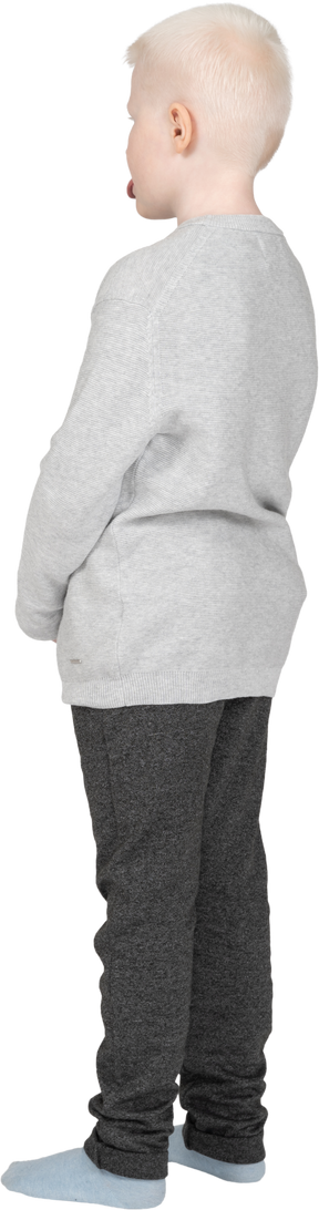 Vista posterior de tres cuartos de un niño en ropa casual mostrando la lengua