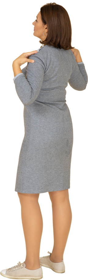 Vista lateral de uma mulher em um vestido cinza em pé com as mãos nos ombros