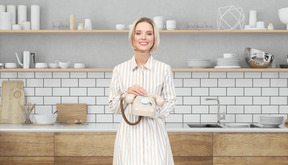 A woman standing in a kitchen holding a rotary dial phone