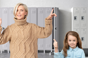 A woman standing next to a little girl in front of lockers