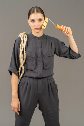 Femme en combinaison grise tenant un rouleau à peinture sur sa joue