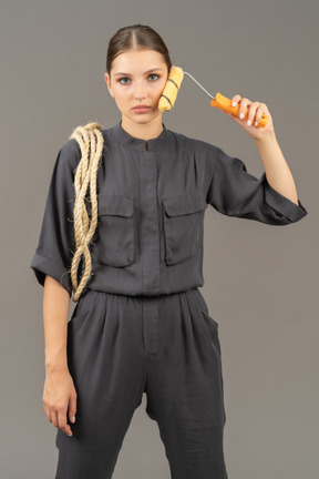 Woman in gray coveralls holding a paint roller to her cheek