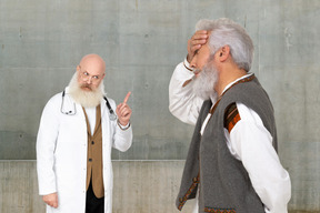 An old doctor pointing finger up and standing next to a man holding his head